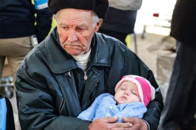 дідусь колихає онуку в центрі біженців